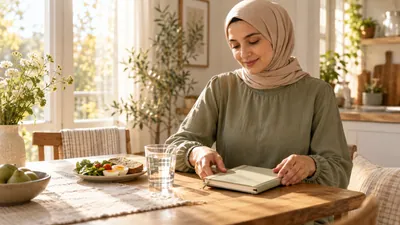 امرأة بملابس محتشمة تنظم دفترها بجانب الماء وإفطار بسيط في صباح هادئ